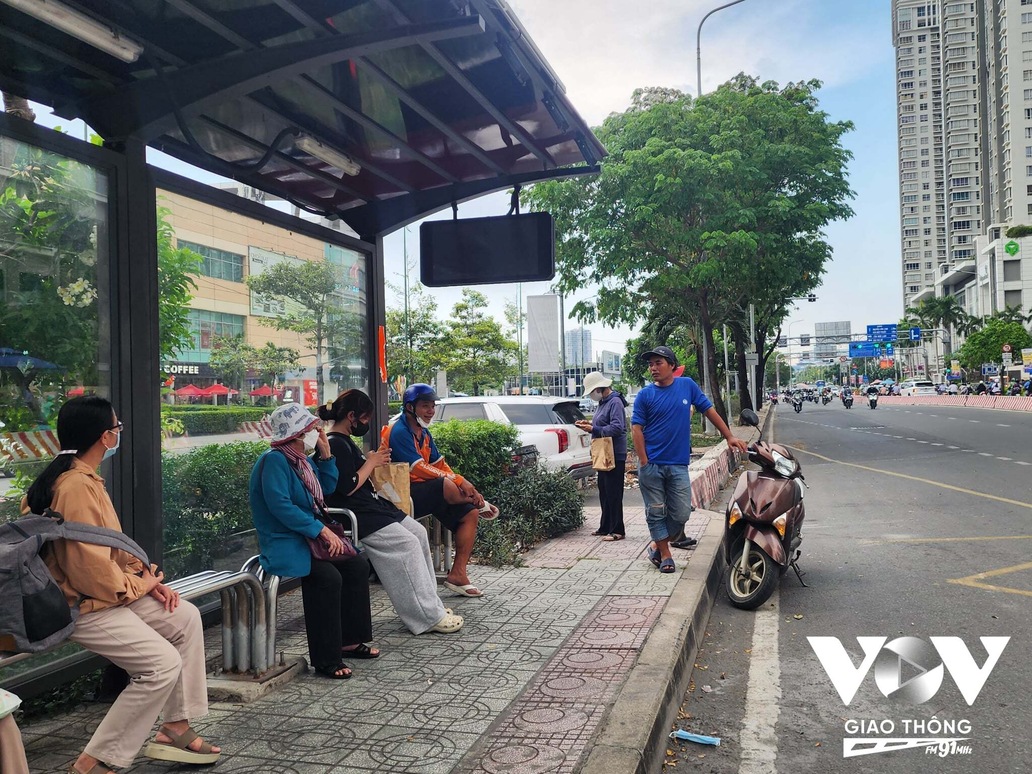 Nhiều hành khách chờ đón xe buýt tại nhà chờ phía trước Trung tâm thương mại Lotte Mart, quận 7