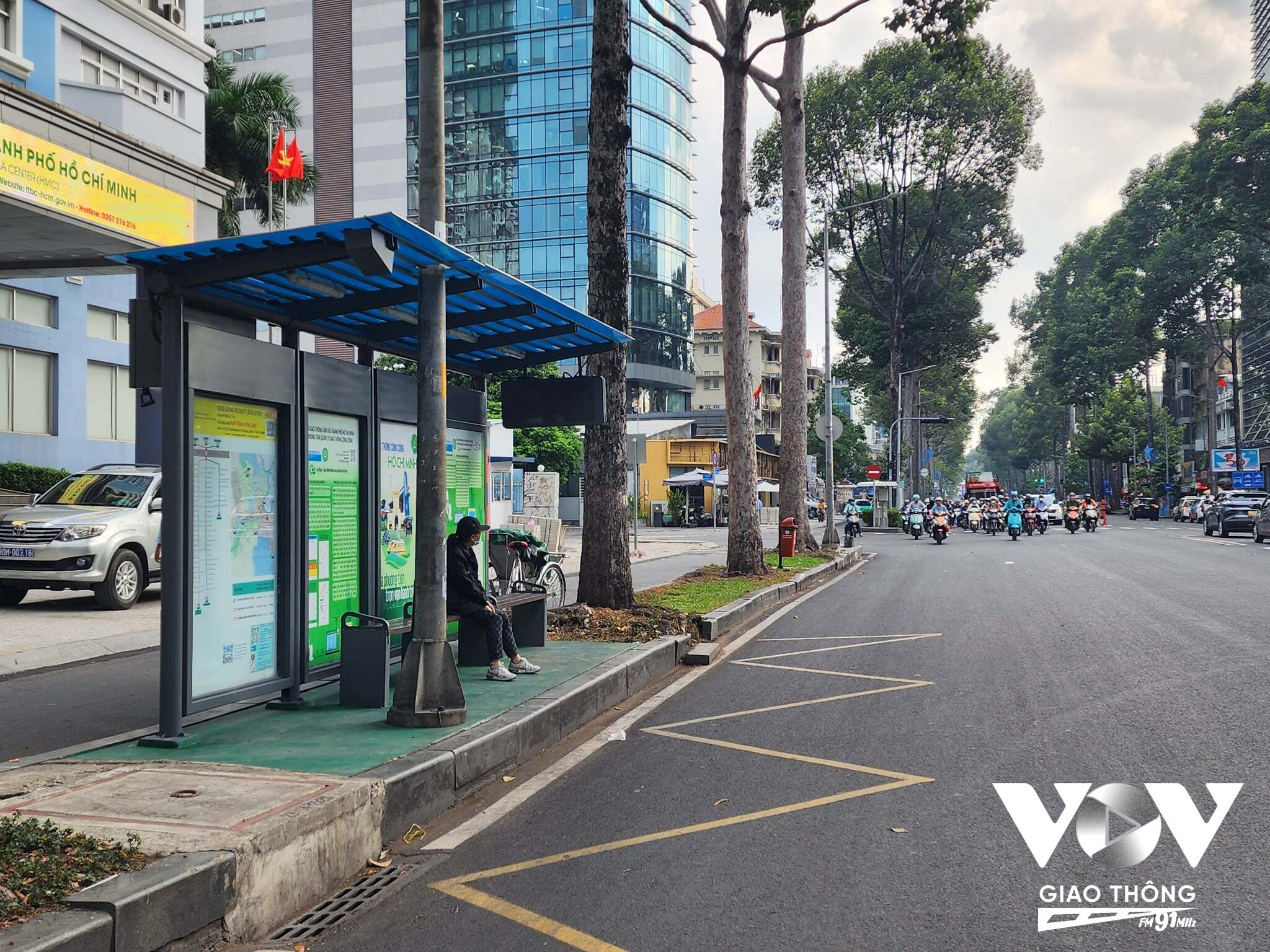 Người dân ngồi chờ xe buýt trong tình trạng thấp thỏm, không biết lúc nào xe sẽ đến nhà chờ xe buýt phía trước Trung tâm Báo chí Thành phố