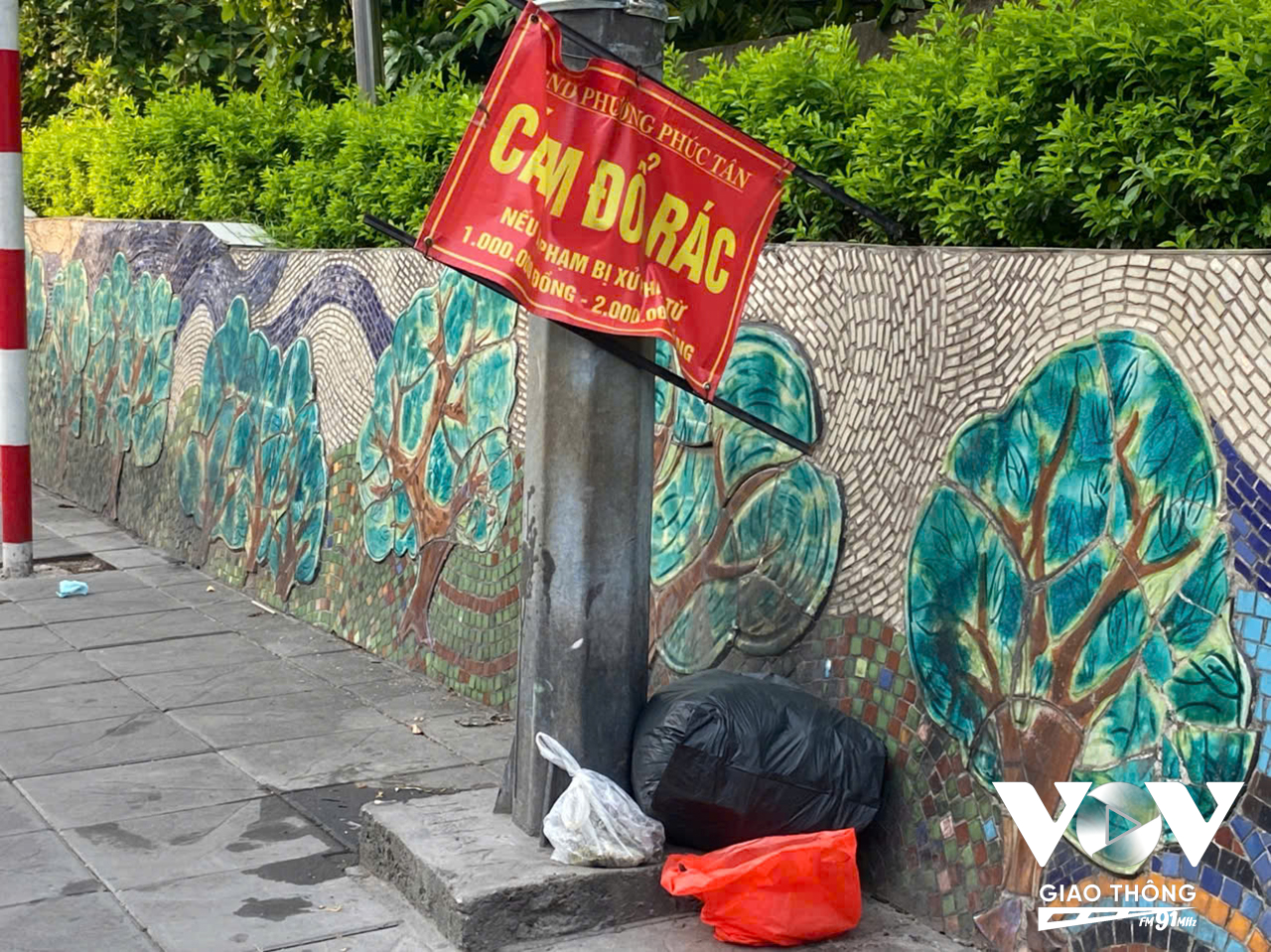 Rác thải chất đống trên vỉa hè, dưới chân bức tranh gốm sứ