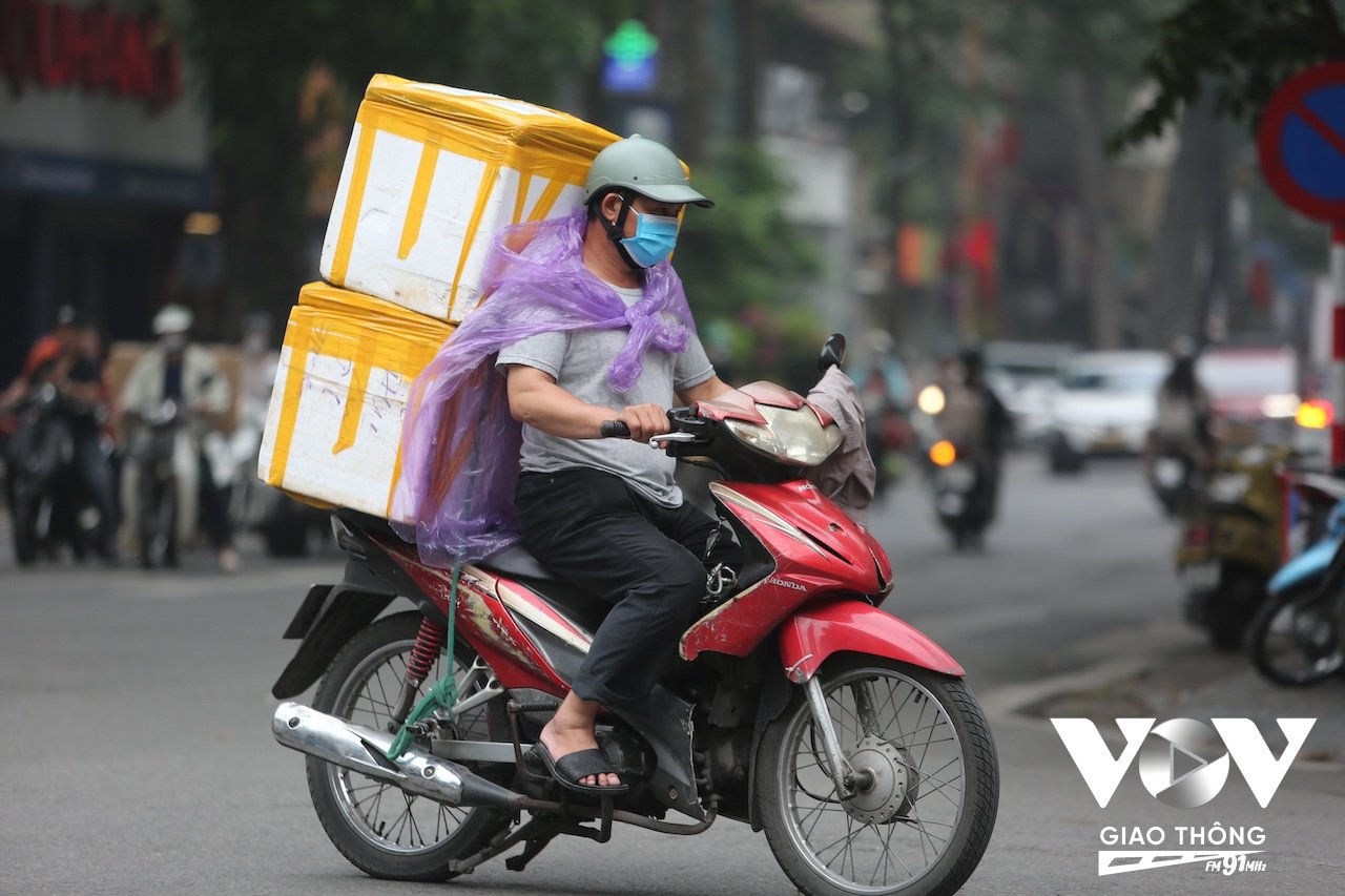 Một người chở hàng phải mặc thêm áo mưa cho đỡ lạnh khi di chuyển trên đường trong sáng sớm nay