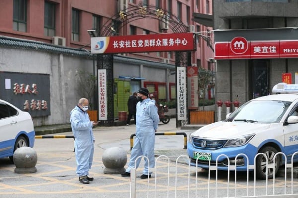 Tài xế taxi mặc đồ bảo hộ, đứng chờ khách trước một khu dân cư ở Vũ Hán.