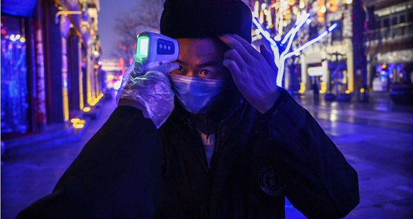 Một công nhân Trung Quốc đeo khẩu trang, tự kiểm tra nhiệt độ trên một con phố thương mại vắng vẻ tại Bắc Kinh.