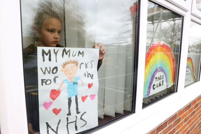 Bé gái dán tấm áp phích lên cửa kính nhà mình để ủng hộ mẹ và Dịch vụ Y tế Quốc gia (NHS), đơn vị tuyến đầu chống dịch Covid-19 tại Anh. (Nguồn: Reuters)