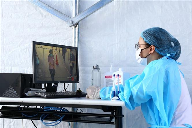 Nhân viên y tế theo dõi máy đo thân nhiệt tự động tại cổng vào của bệnh viện Bạch Mai. Ảnh: Minh Quyết/TTXVN