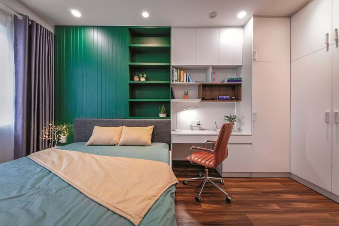 Sự kết hợp giữa bàn làm việc, kệ sách và tủ quần áo thành một cụm không gian liên đới giúp cho phòng ngủ có vẻ rộng rải hơn so với diện tích khiêm tốn vốn có.