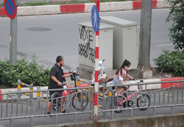  Một người đàn ông đang bê xe đạp cho hai cháu nhỏ qua hàng rào để vào bên trong tập xe.