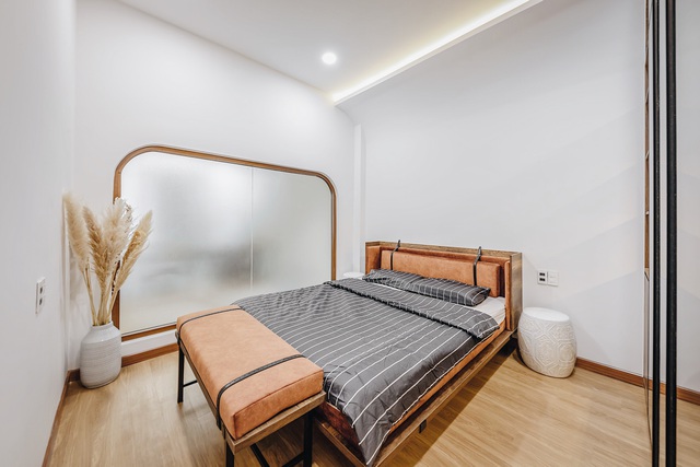 Nội thất tối giản nhưng sang trọng với hệ tủ gỗ cách điệu, bắt mắt. Giường ngủ tạo điểm nhấn với phần bọc nệm màu cam. Trên đầu giường bố trí 2 đôn sứ để vật dụng, đèn, sách và điện thoại khá hữu ích.