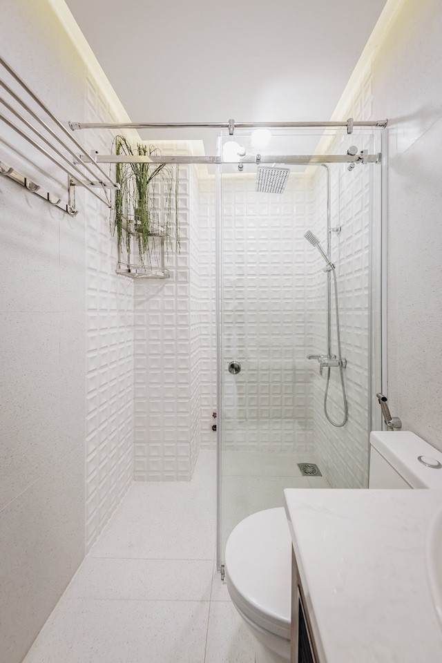 Nhà vệ sinh tone trắng chủ đạo với khu vực tắm đứng riêng biệt và nhấn nhá bởi mảng tường phía sau, tạo cảm giác không gian sạch sẽ và rộng rãi.